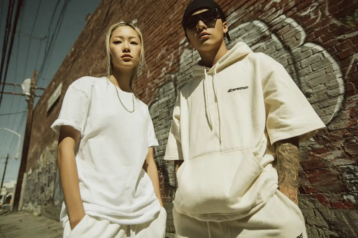 Two young adults in matching white streetwear outfits.
